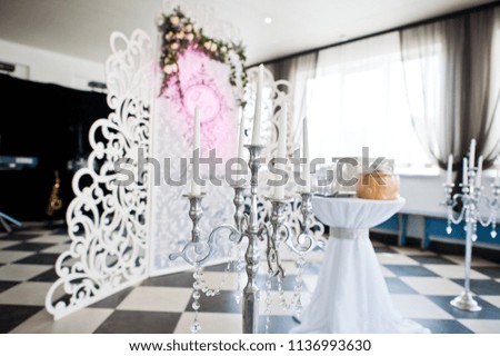 Special photo zone with small wooden wall decorated with flowers and wedding couple's initials. Table with box and bread on it.