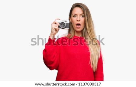 Beautiful young woman holding vintage camera scared in shock with a surprise face, afraid and excited with fear expression