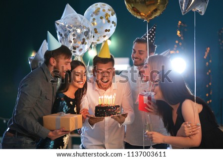 Young man with friends and birthday cake in club