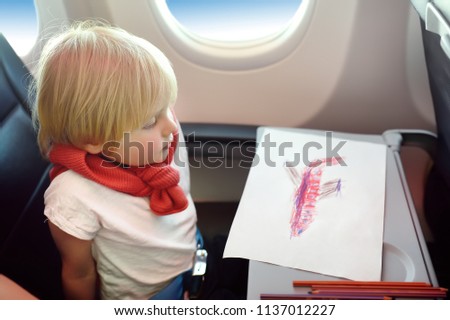 Charming kid traveling by an airplane. Joyful little boy sitting by aircraft window during the flight. Air travel with little kids