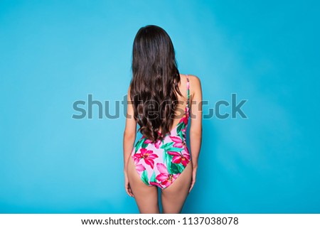 Back view photo of young woman in colorful swimsuit with flowers picture posing on blue background. Summer and vacation