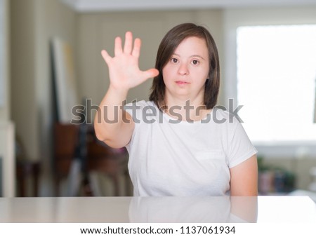 Down syndrome woman at home with open hand doing stop sign with serious and confident expression, defense gesture