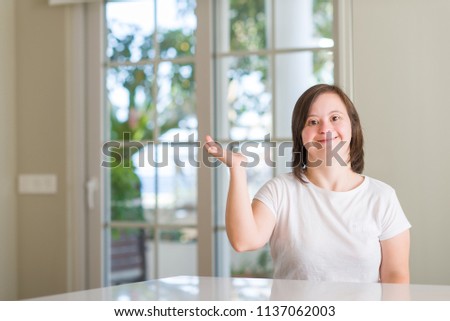 Down syndrome woman at home smiling cheerful presenting and pointing with palm of hand looking at the camera.