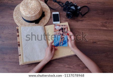 girl's hands and photo album, photo camera, phone, straw hat and on a wooden background, close-up