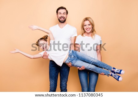 Cheerful smiling bearded father and blonde happy mother carring their little daughter offspring in their arms on beige background