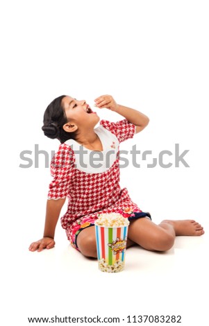 Cute little Indian/asian girl eating popcorn, isolated over white background

