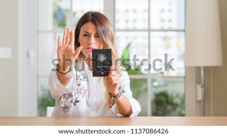 Young woman at home holding a passport of Australia with open hand doing stop sign with serious and confident expression, defense gesture