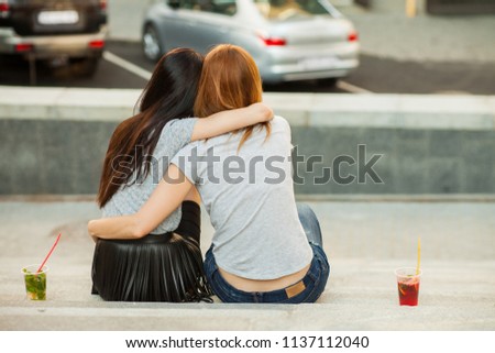 two girls hugging and drink cold cocktails, pretty friends, nice girlfriends walk around the city and drink lemonade. back view Royalty-Free Stock Photo #1137112040