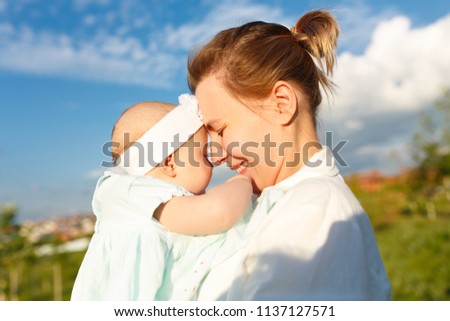 Warm, gentle and heartwarming photo of a young mother hugging her little daughter in the park at sunset of the day. Beautiful sky and green trees around them. Love, close up, family lifestyle