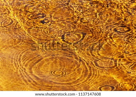 Rain drops falling into shallow water with golden sand.
