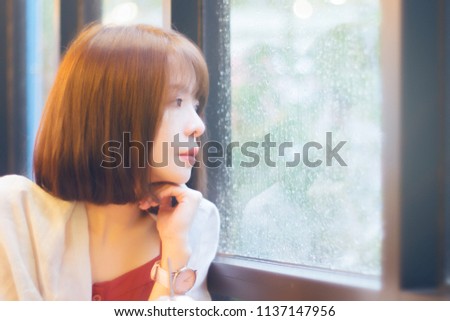 attractive cute asian young girl looked outside window at raining moment. cute asian woman short hair with blurred background. romantic concept. light effect added. filtered image to vintage tone. 
