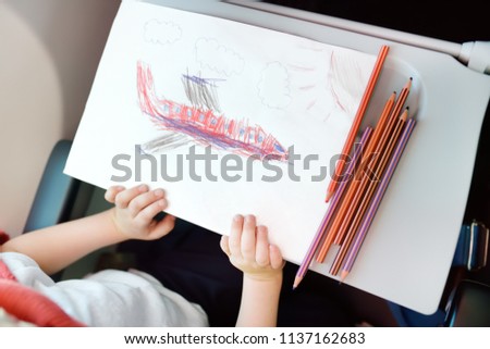 Child traveling by an airplane. Kid drawing aircraft during air trip. Little boy during travel with his family