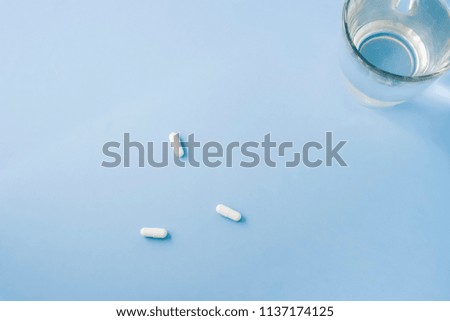 Three white pills and a glass of fresh water on pastel blue table. Flat lay, top view, space for text.