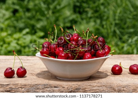 Bowl with fresh cherry on rustic wooden table outdoor