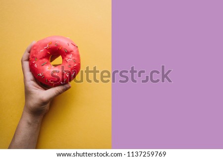 A girl is holding a donut on a colored background. Nearby place for text