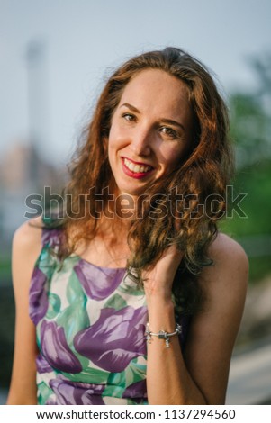 Portrait head shot of a young, beautiful and attractive European woman wearing a floral print dress during sunset. She is smiling warmly and genuinely. 