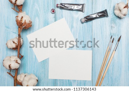 preparation for creativity - sheets of paper, drawing. top view of the working manages on a blue wooden background with paints, brushes and cotton flowers. flat lay