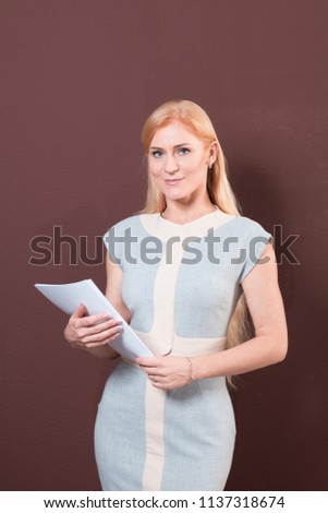 Young blonde woman in blue dress is holding paper in hands
