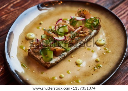 Smorrebrod Danish sandwich with salmon fish, curd mousse, marinated cucumber and radish. Delicious vegetarian snack food with dark rye bread and different topping and wine glass at restaurant table