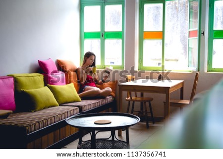 Young woman sitting in front of a window drinking a cup of coffee concentrated reading a book.