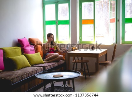 Young woman sitting in front of a window drinking a cup of coffee concentrated reading a magazine. 