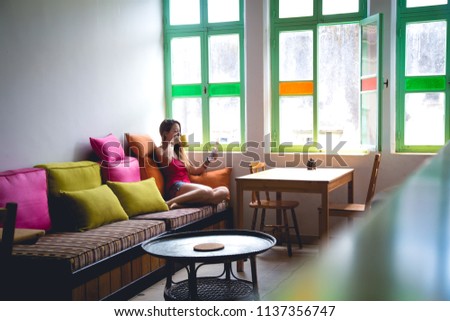 Young woman sitting in front of a window drinking a cup of coffee surprised reading the news.