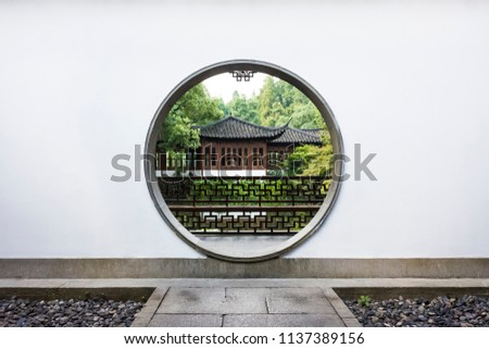 Traditional Chinese house among trees viewed through a circular moon gate and white wall in Guo's Villa (Guo Zhuang), a traditional Chinese Garden near West Lake, Hangzhou, China Royalty-Free Stock Photo #1137389156