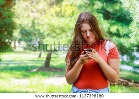 Cute teenager girl using a smart phone in a park with a green background