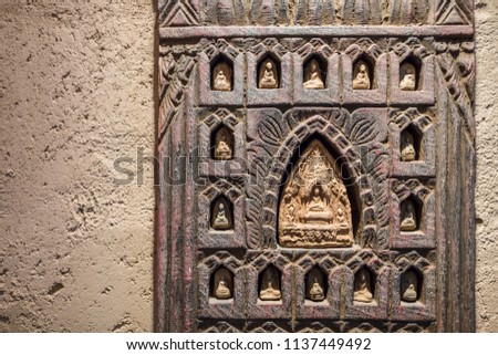 Buddhist wooden carving on a yellow plaster wall with copy space religious artifacts with light from above casting shadows temple art