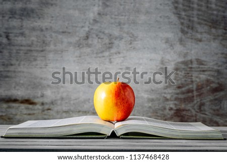 Red apple on open book with gray wooden background