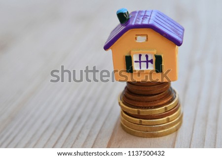 Property investment, house mortgage and money saving financial concept with copy space for text. Colorful house on money coin stack on natural blurred wood background.
