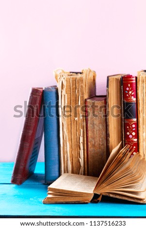 Stack of old books with open one close up on blue wooden shelf, copy space on pink wall background