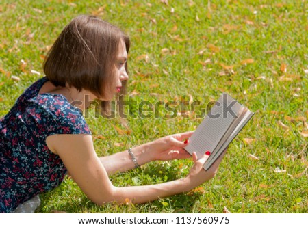 Pretty woman with red lips reading a book and lying on green grass in warm sunny day