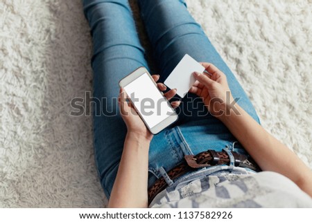 Young woman holding credit card and using phone sitting on floor. Payment.  Online shopping concept.Concept of blogging. Modern technologies Top view.