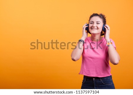 Beautiful young woman listening music with her headphones on yellow background