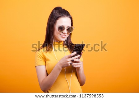 Cute young woman texting on her phone wearing glasses in studio on yellow backgroud