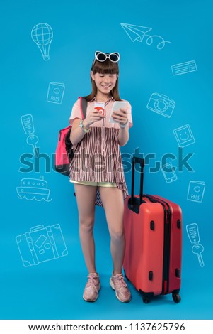 Easy shopping. Positive progressive teenager smiling and standing near a big suitcase while shopping online before starting the journey