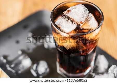 Cola with ice cubes and bubbles in glass, top view.