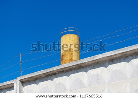 Concrete fence with barbed wire on blue sky background. High yellow tower on a high fence.