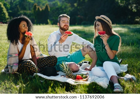 Picnic of three multi race friends. Beautiful african woman and her caucasian male and female friends are enjoying the watermelon.