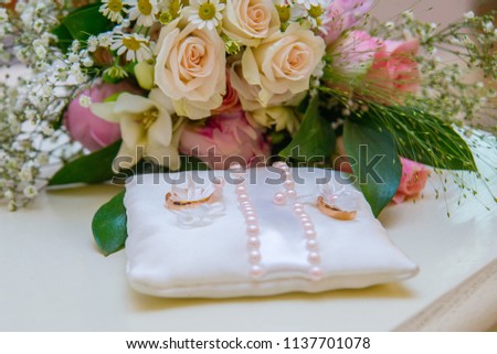 Two gold rings are on the wedding pillow. Beautiful flowers on your wedding day. Bouquet of roses of daisies