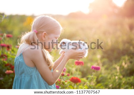 beautiful little girl holding in hands white rabbit at the garden

