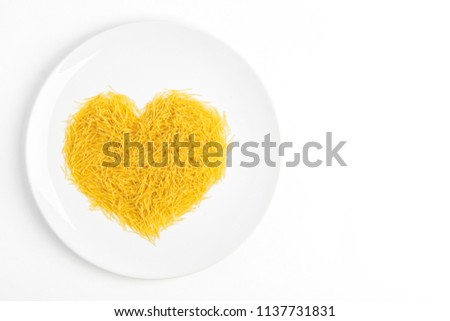 Close up of short and thin dry Italian vermicelli heart. Yellow raw or fresca wheat pasta heart shaped on whit plate on white background. Love pasta concept, free copy space for text