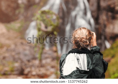 Woman tourist or photographer taking photo of waterfall with digital camera 