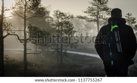 Photographer men with camera and tripod walks through foggy swamp at morning Royalty-Free Stock Photo #1137755267