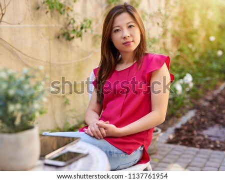 Portrait of a smiling young Asian woman relaxing outside at her patio table on a sunny day 