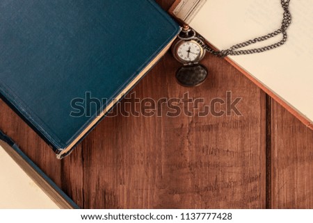 An overhead photo of old books, shot from above on a dark background with a vintage chain watch and copy space