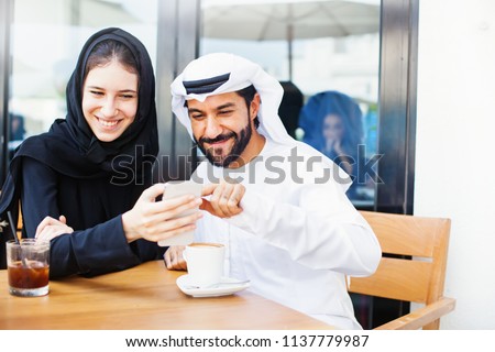 Happy arab middle eastern couple using mobile phone and drinking coffee