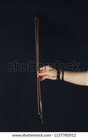 In the hand of an adult male bow from a violin musical instrument on a black isolated background.