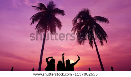 Silhouette of Friends taking Selfie via Smartphone at the Beach during Sunset. Tropical Coconut Trees and Twilight Sky as background
